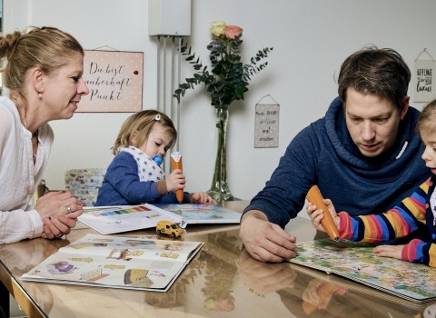 Kinderbetreuung zu Hause, zwei Erwachsene spielen mit zwei Kindern an einem Tisch und betreuen diese.